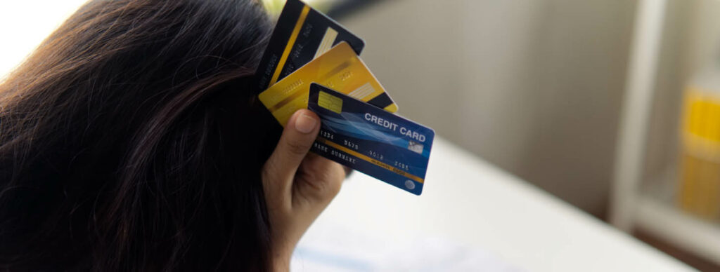 person holding multiple credit cards up to their head, contemplating financial decisions