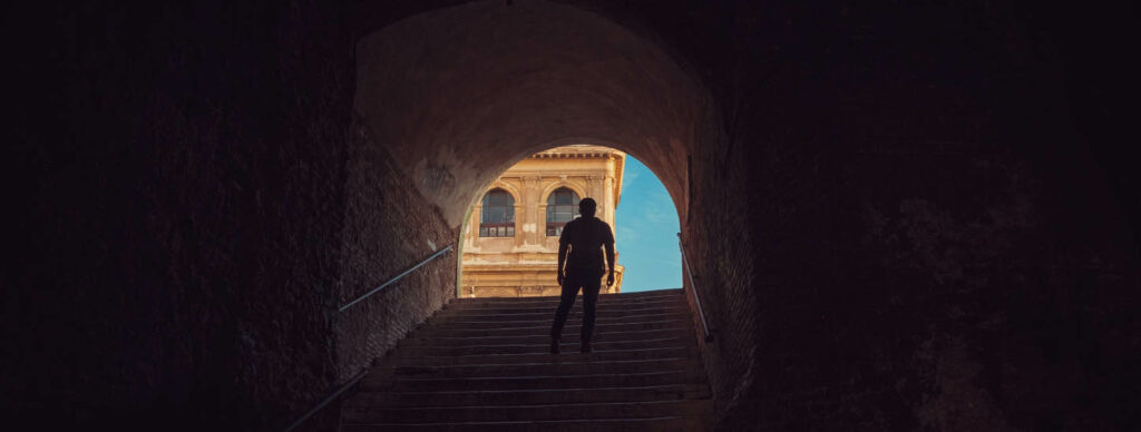 a person walking up the stairs towards the light at the end of a tunnel
