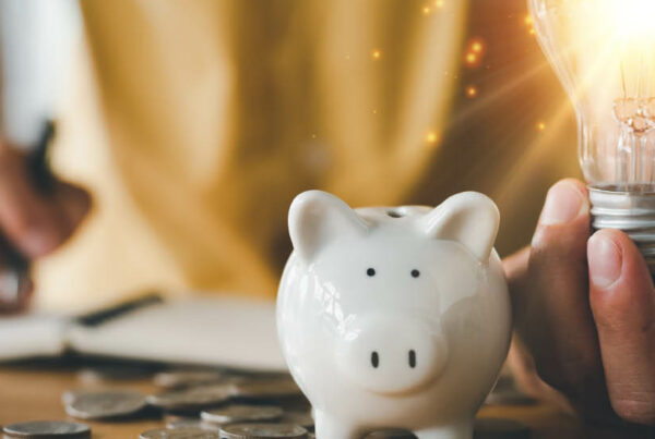 person writing in a notebook with a piggy bank and a bright lightbulb in hand