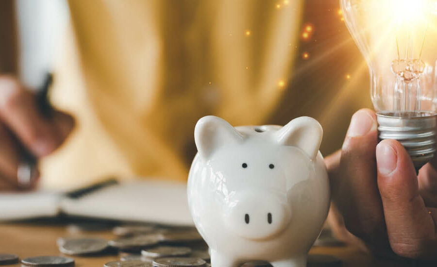 person writing in a notebook with a piggy bank and a bright lightbulb in hand